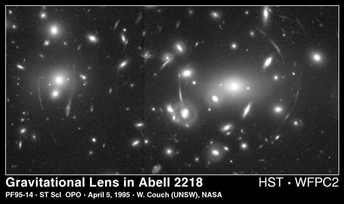  NASA     ЭФФЕКТ ГРАВИТАЦИОННОГО ЛИНЗИРОВАНИЯ, вызванный большой массой вещества в скоплении галактик Абель 2218. Наблюдаемая сквозь него более далекая галактика представляются нам в виде светлых дуг, огибающих центральную часть скопления; фактически это сложное